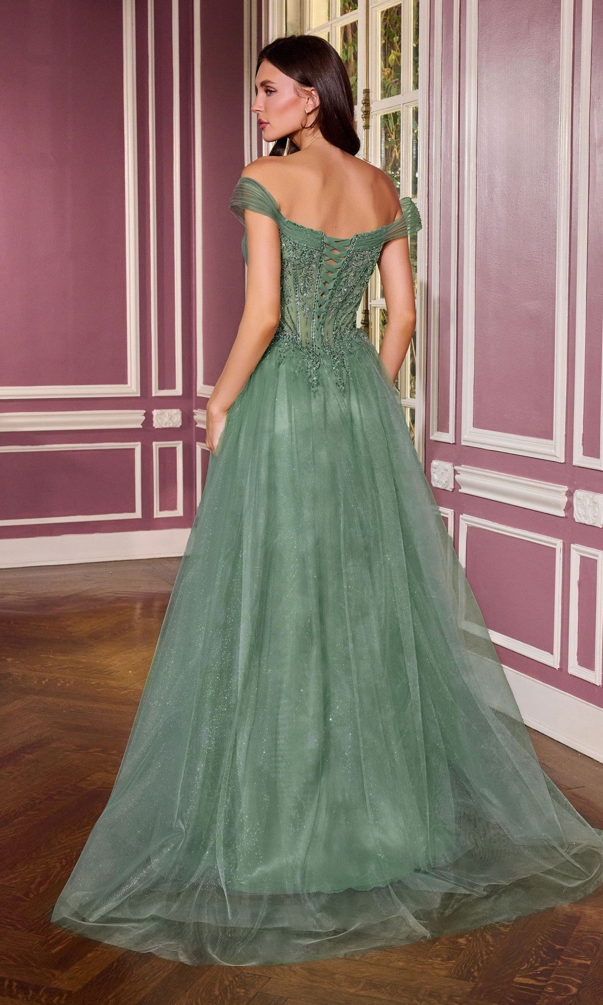 A woman stands in an ornate room, facing away from the camera, wearing the Ladivine CC493 Long Prom Dress—a floor-length green gown with an off-shoulder sweetheart neckline, fitted bodice, and tulle skirt.